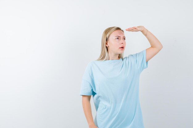 Mujer rubia mirando lejos con la mano por encima de la cabeza en camiseta azul y mirando enfocado