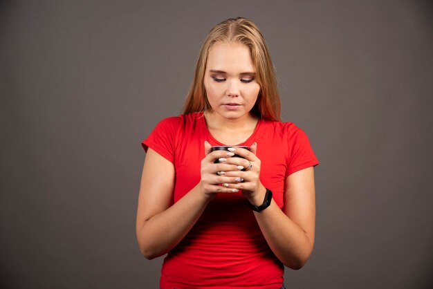 Mujer rubia mirando una taza de té en la pared negra.