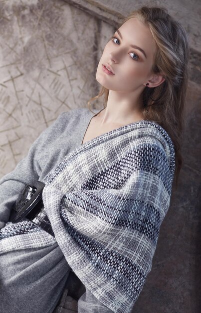 Mujer rubia de moda con un vestido gris posando en un interior artístico.