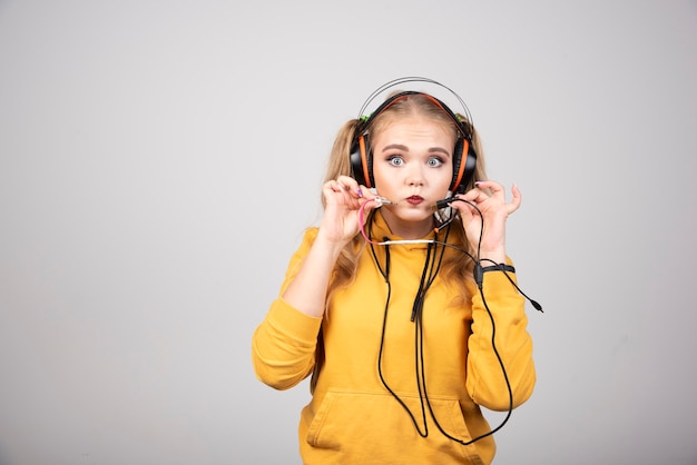 Mujer rubia mostrando auriculares sobre fondo gris.