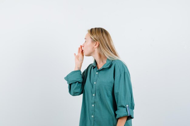 Mujer rubia mostrando delicioso gesto en camisa verde y mirando encantada.