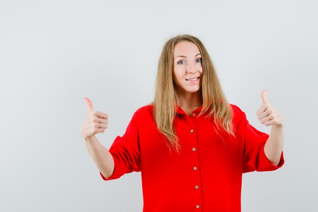 Mujer rubia mostrando doble pulgar hacia arriba en camisa roja y mirando contenta.