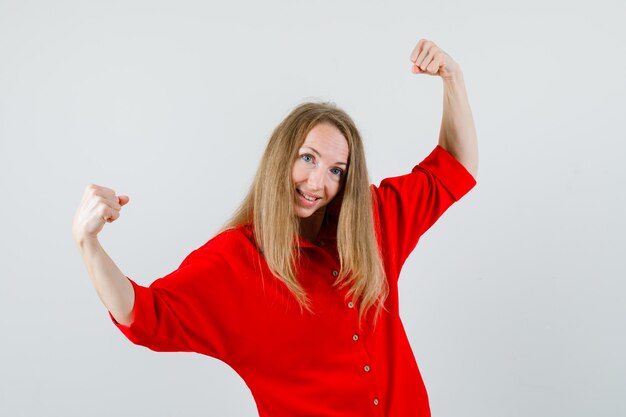 Mujer rubia mostrando gesto de éxito en camisa roja y mirando feliz,