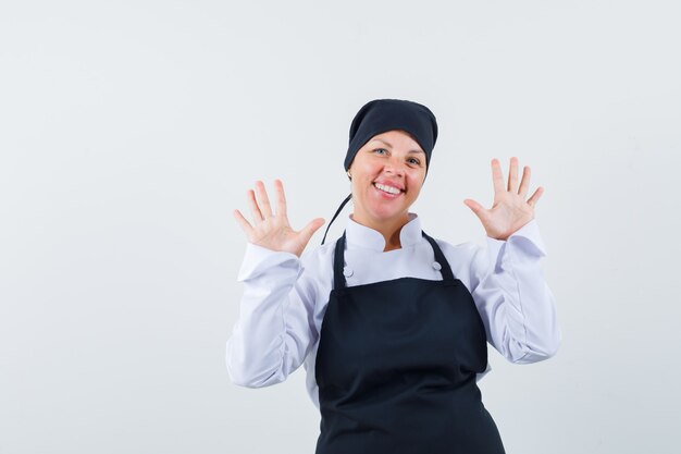 Mujer rubia mostrando gestos de parada en uniforme de cocinero negro y bonita.