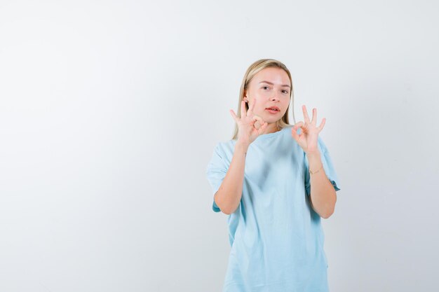 Mujer rubia mostrando signos de ok en camiseta azul y mirando confiado