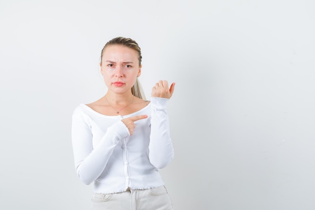 La mujer rubia muestra qué hora es en el fondo blanco