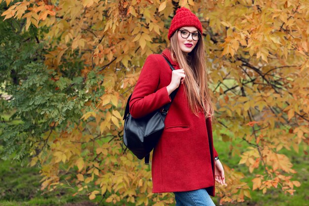 Mujer rubia con pelos largos caminando en el soleado parque de otoño en traje casual de moda.