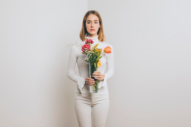 Mujer rubia pensativa con flores brillantes en florero