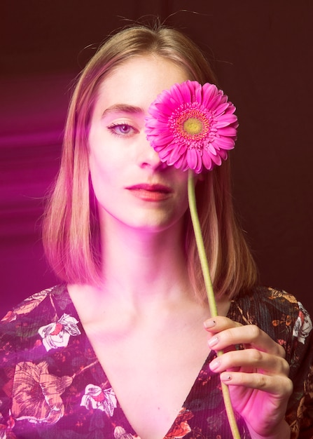 Mujer rubia pensativa con gerbera rosa