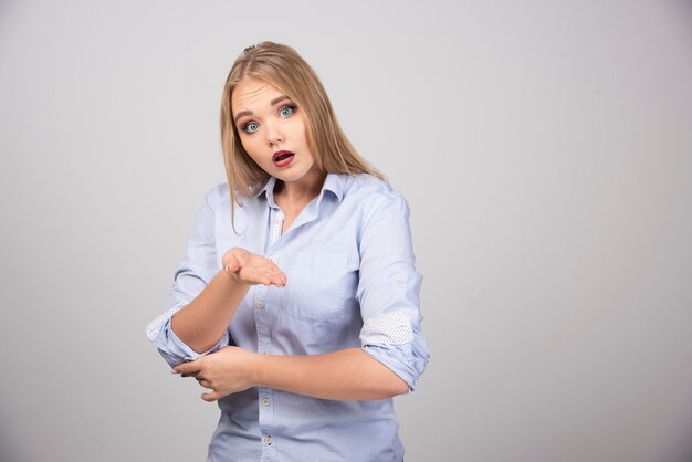 Mujer rubia de pie con la boca abierta y mostrando la palma.