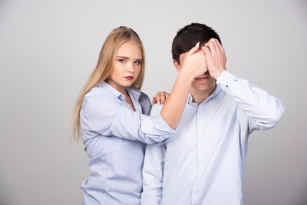 Mujer rubia de pie y cerrando los ojos al modelo de chico en camiseta blanca