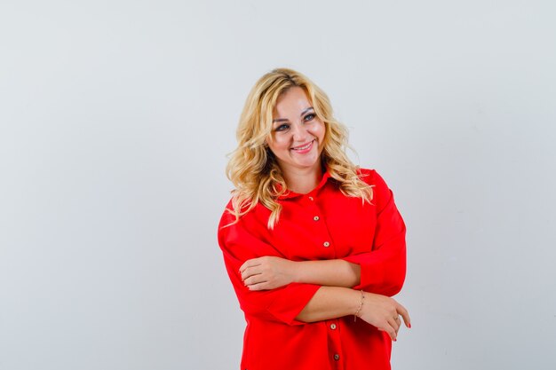 Mujer rubia de pie con la espalda recta y posando a la cámara en blusa roja y mirando feliz