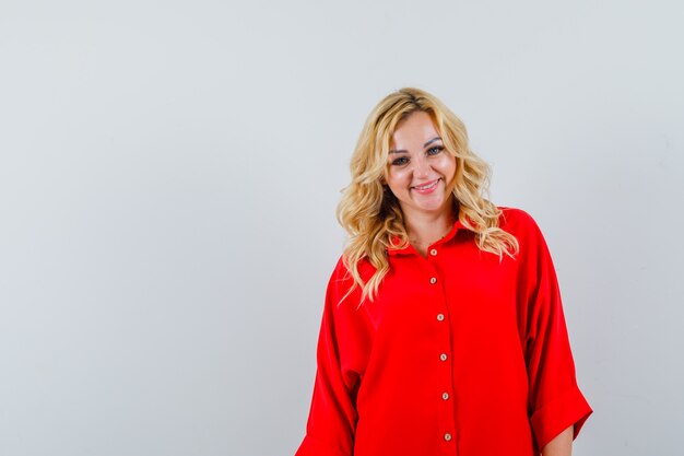 Mujer rubia de pie con la espalda recta y posando a la cámara en blusa roja y mirando feliz