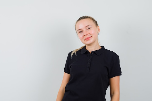 Mujer rubia de pie con la espalda recta y sonriendo en camiseta negra y mirando feliz