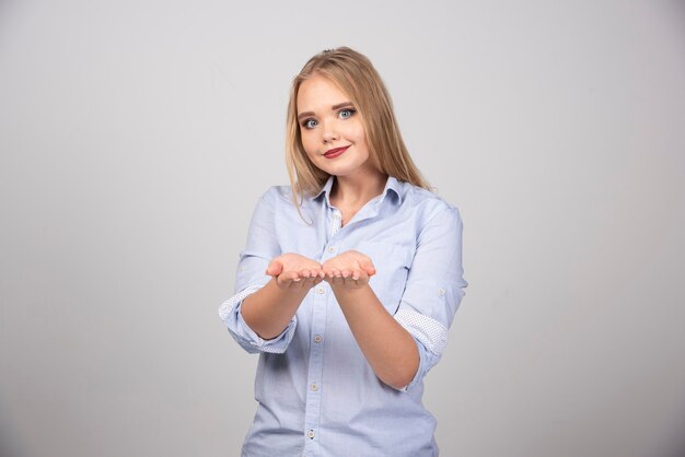 Mujer rubia de pie y mostrando las palmas abiertas contra la pared gris.