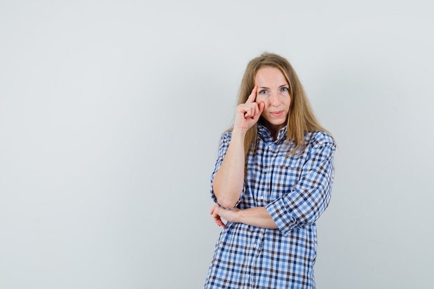 Mujer rubia de pie en pose de pensamiento en camisa y mirando sensible,