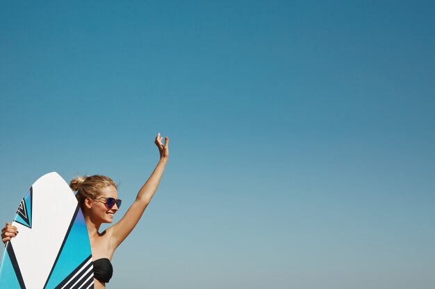 Mujer rubia en la playa con tabla de surf