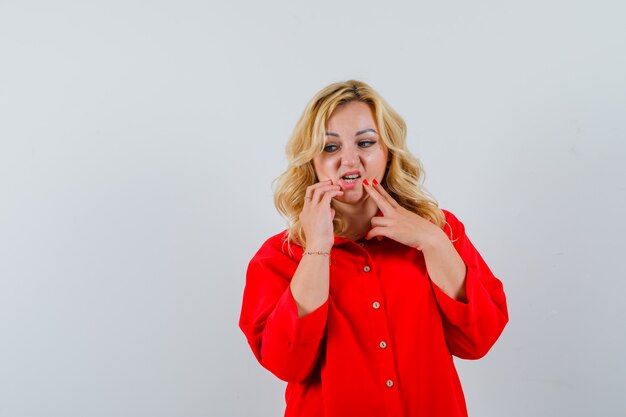 Mujer rubia poniendo los dedos en la barbilla, pensando en algo en blusa roja y mirando pensativo,