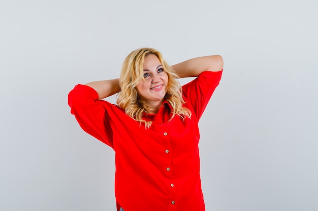 Mujer rubia poniendo las manos en la cabeza en blusa roja y mirando feliz.