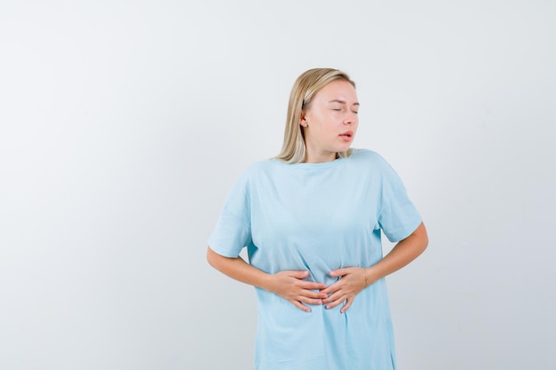 Mujer rubia poniendo las manos sobre el vientre, con dolor de estómago en camiseta azul