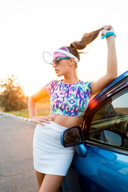 Mujer rubia posando junto al coche con elegante traje de verano.