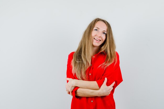 Mujer rubia posando mientras está de pie en camisa roja y mirando alegre,