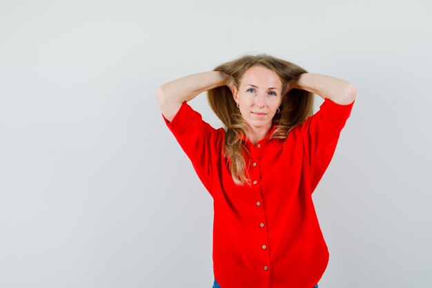 Mujer rubia posando mientras junta la cabeza con las manos en camisa roja y mirando seductor,