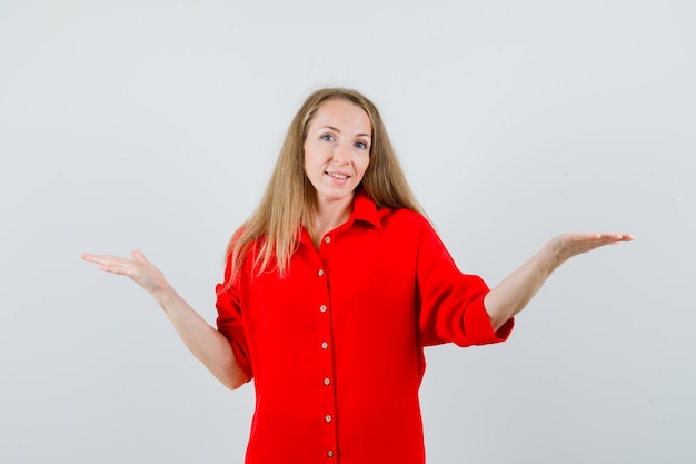 Mujer rubia presentando o comparando algo en camisa roja y mirando alegre.