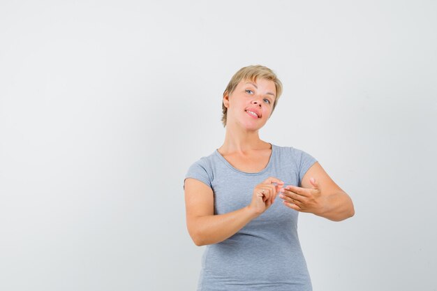 Mujer rubia que finge escribir algo en una camiseta azul claro y luce optimista, vista frontal.