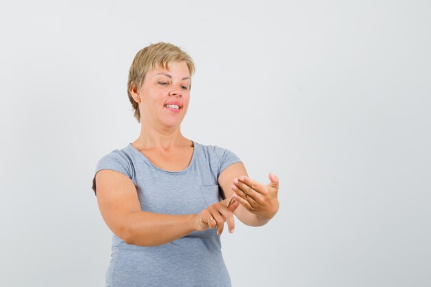 Mujer rubia que finge escribir algo en una camiseta azul claro y mira enfocada, vista frontal.