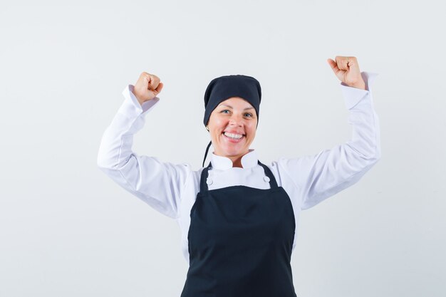 Mujer rubia que muestra el gesto del ganador en uniforme negro del cocinero y que parece feliz.