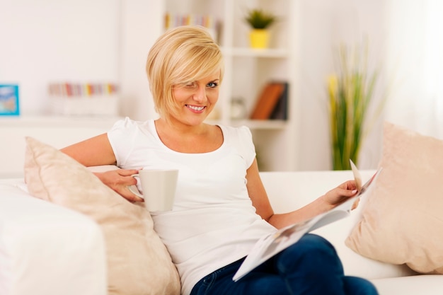 Mujer rubia relajándose en casa con café y periódico