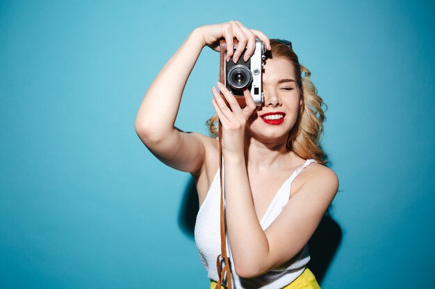 Mujer rubia en ropa de verano tomando fotos en cámara retro