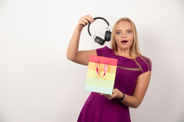 Mujer rubia sacando auriculares de la bolsa con expresión feliz.