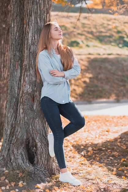 Mujer rubia segura descansando en un árbol