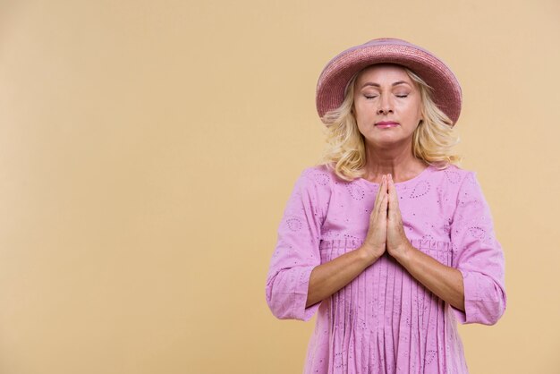 Mujer rubia senior con sombrero rosa rezando