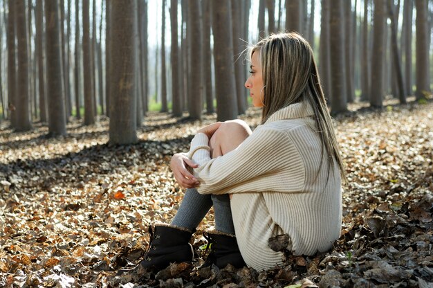 Mujer rubia sentada sobre hojas en un bosque