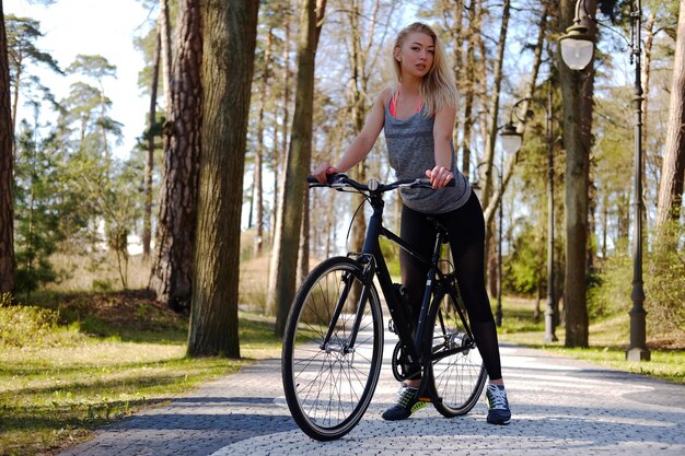 Mujer rubia sexy posando junto a la bicicleta en un parque de verano.