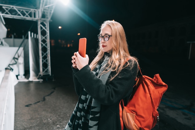 Mujer rubia con smartphone en la noche en la calle.