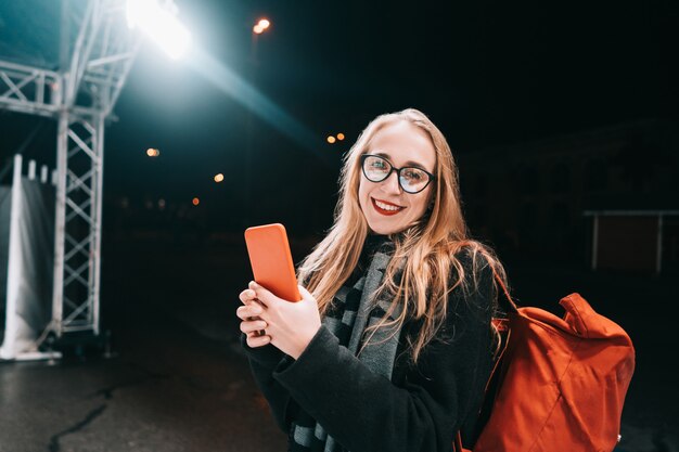 Mujer rubia con smartphone en la noche en la calle.