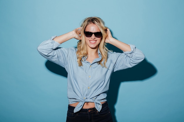 Mujer rubia sonriente en camisa y gafas de sol posando