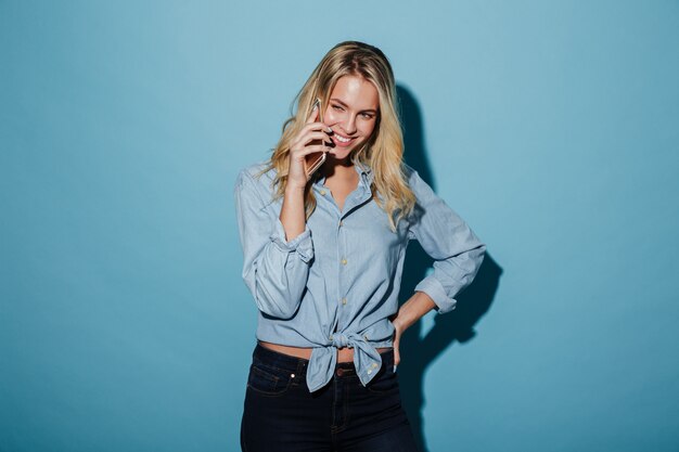 Mujer rubia sonriente en camisa hablando por teléfono inteligente