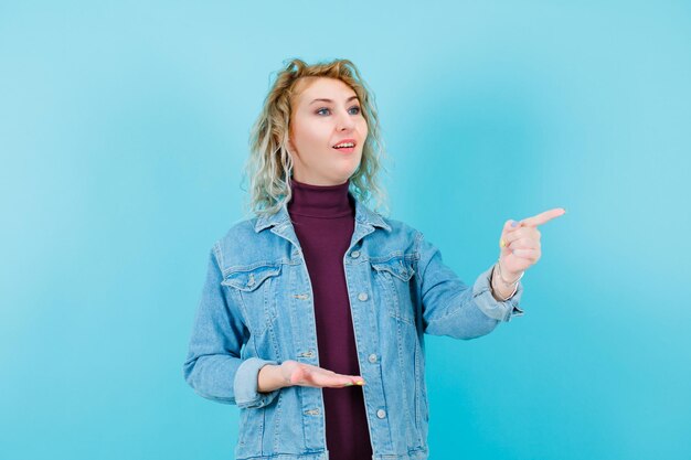 Mujer rubia sonriente está apuntando con el dedo índice sobre fondo azul.