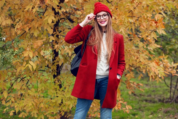 Mujer rubia sonriente con pelos largos caminando en el soleado parque de otoño en traje casual de moda.