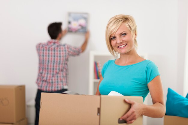 Mujer rubia sonriente sosteniendo una caja de cartón durante la mudanza