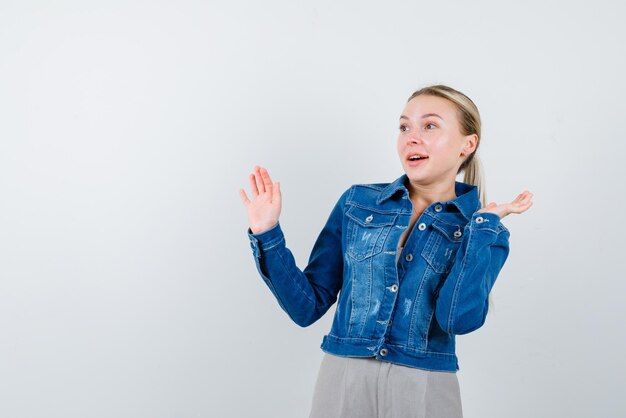 La mujer rubia sorprende al levantar las manos sobre fondo blanco.