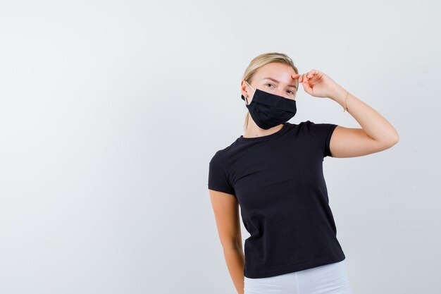 Mujer rubia sosteniendo la mano sobre la cabeza mientras posa en camiseta negra