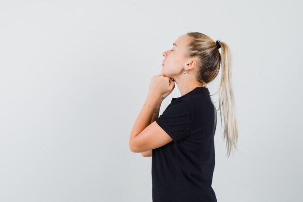 Mujer rubia sosteniendo sus manos debajo de la barbilla en camiseta negra y mirando relajado