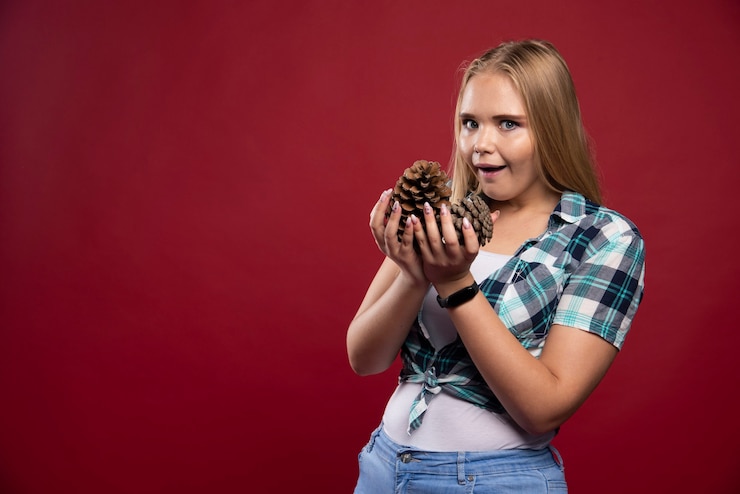 Foto gratuito mujer rubia sostiene el cono de roble en la mano y da poses de sorpresa.