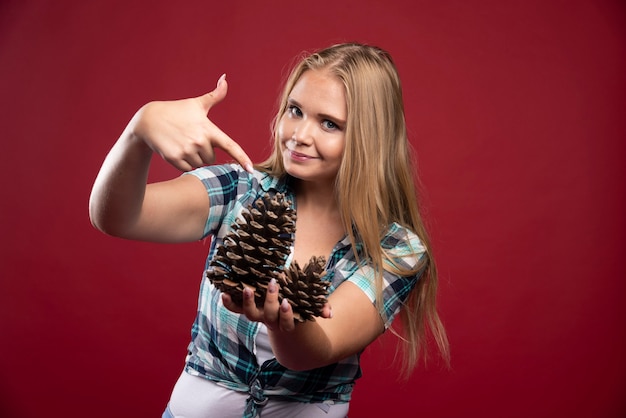 La mujer rubia sostiene el cono de roble en la mano y se ve positiva y alegre.